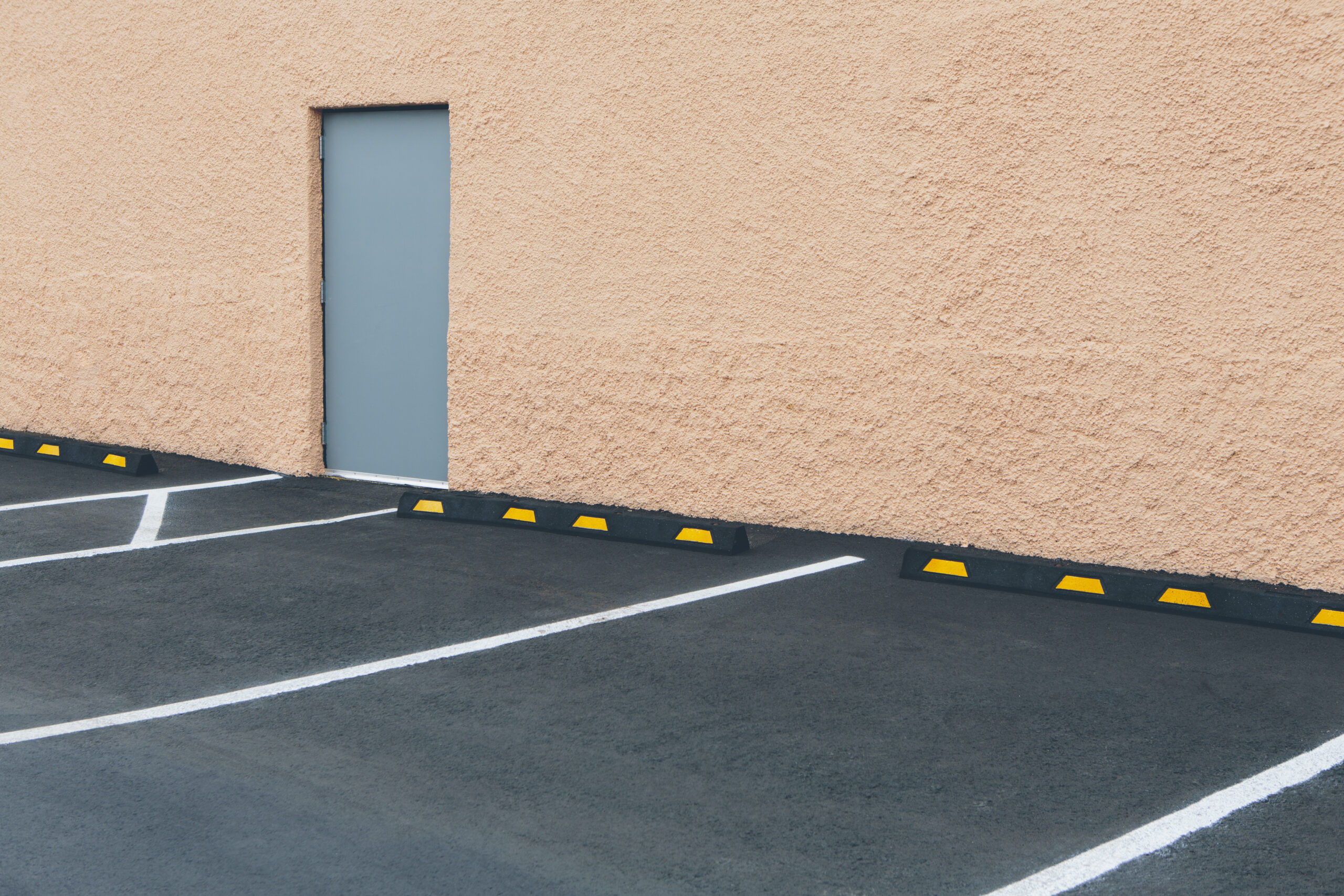 A car park with lined bays outside a building, and a door in a wall. ,Sante Fe,USA